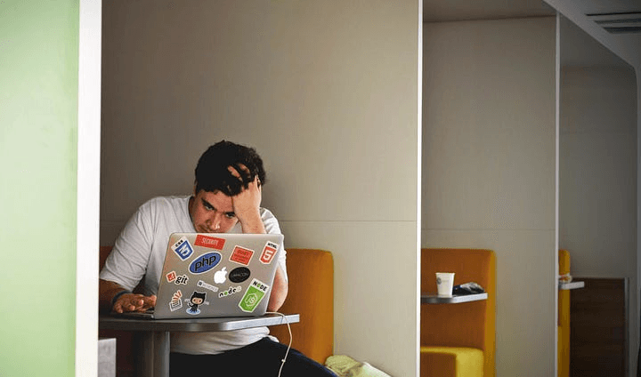 Man working in front of a laptop, looking very tensed.