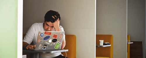 Man working in front of a laptop, looking very tensed.